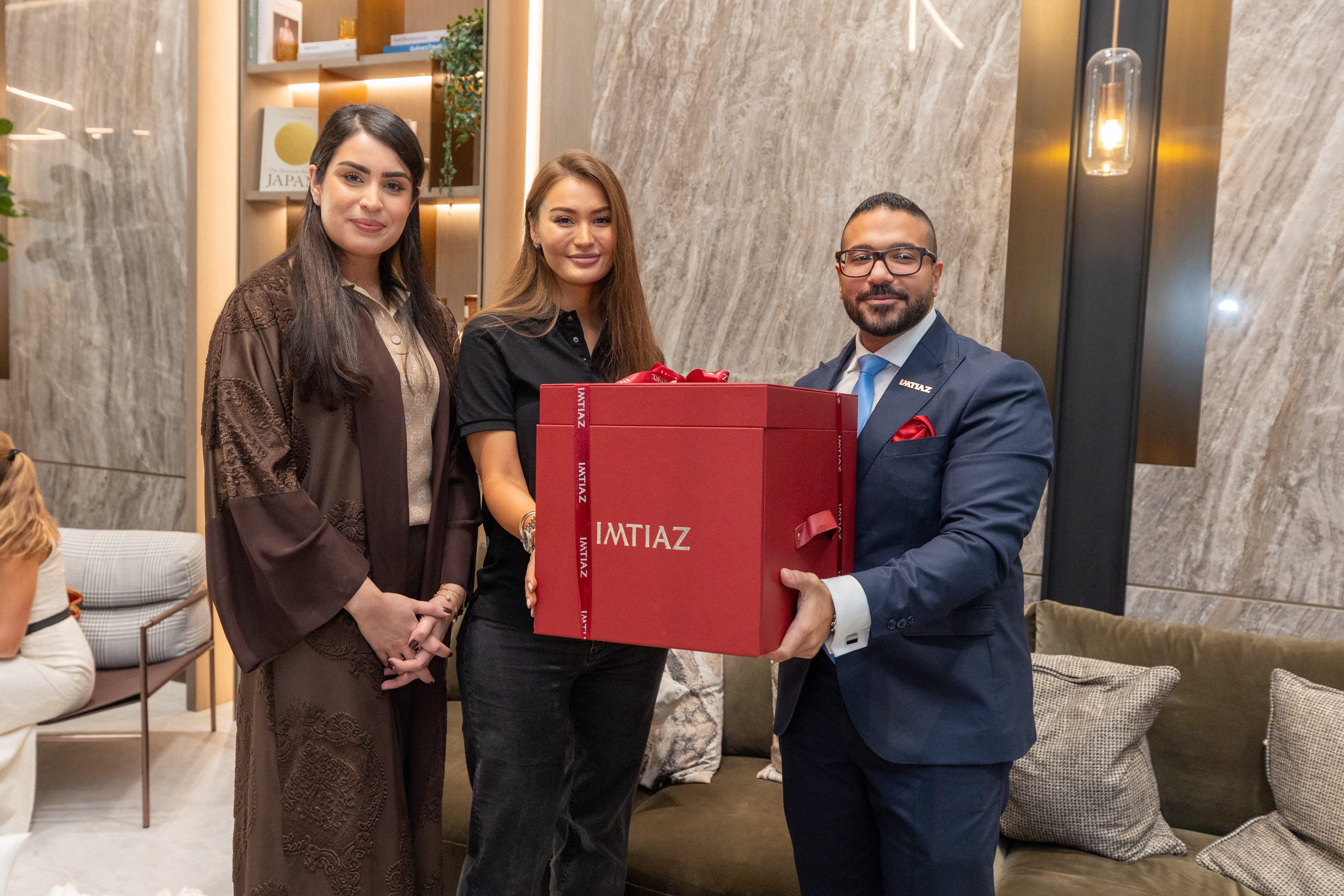 Events?Page=4 A pair of silver scissors with a red ribbon bow, placed on red paper featuring the word "IMTIAZ" repeatedly.