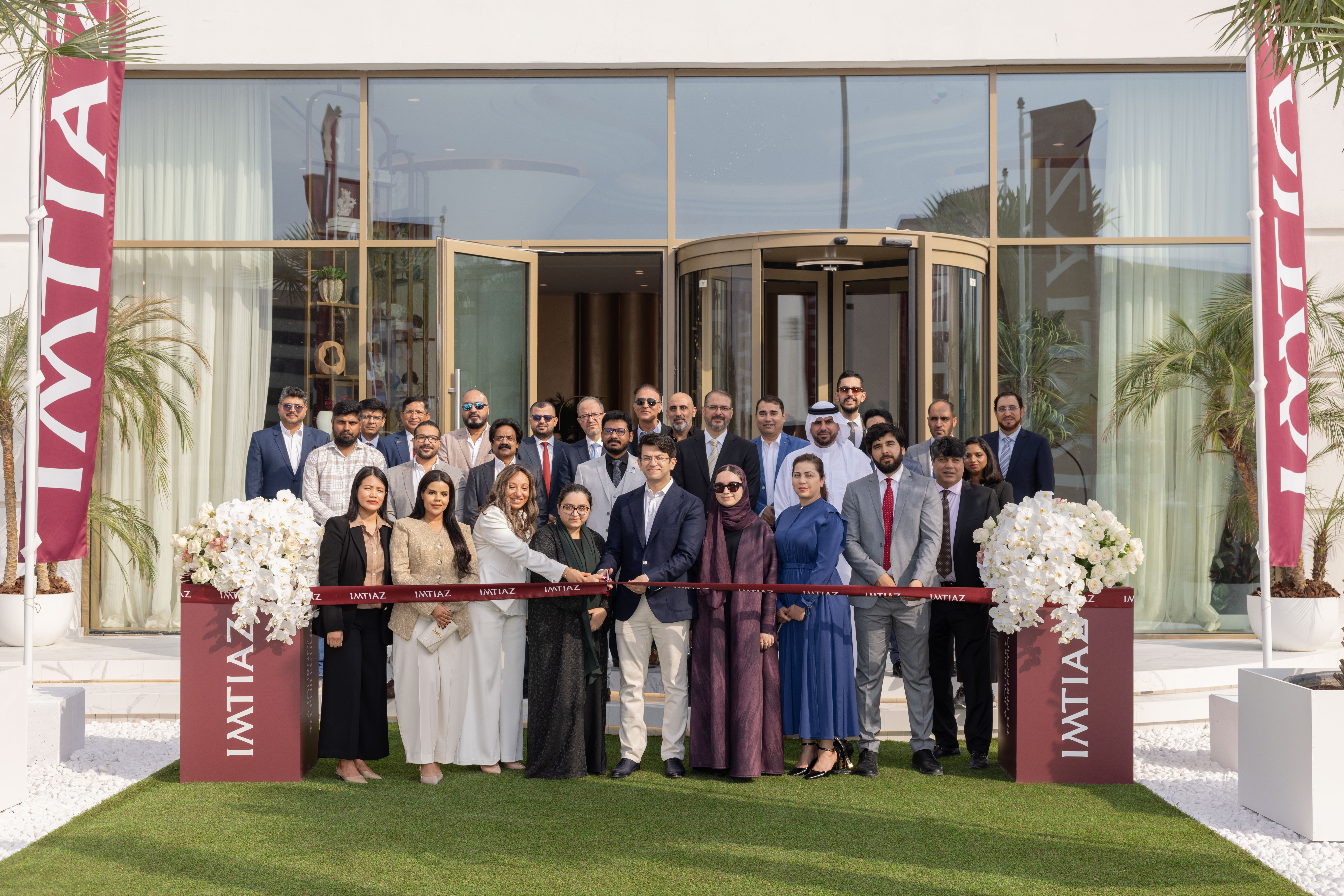 Events?Page=2 Group of people celebrating a ribbon-cutting event, with an "IMTIAZ" banner and decorative flowers in view.