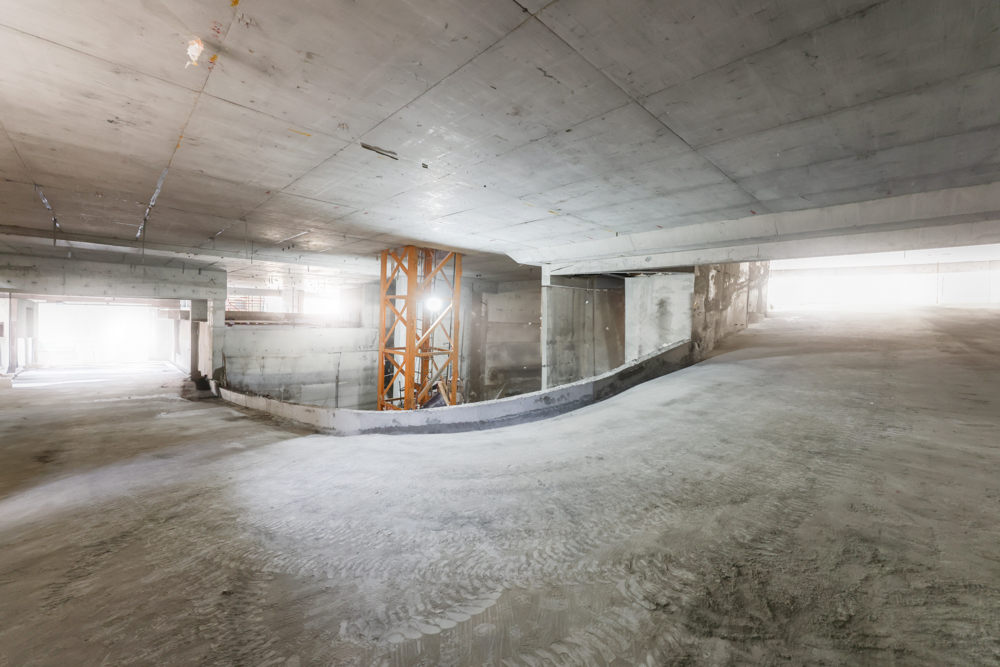 Pearl House By Imtiaz A spacious, unfinished concrete parking garage with an orange construction lift and bright overhead lights.