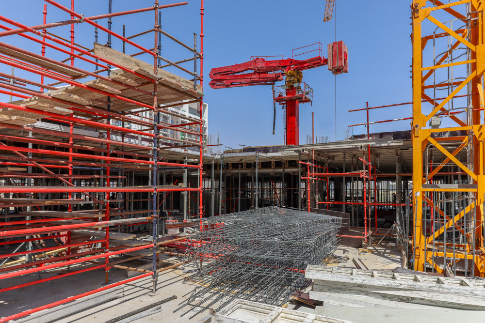 Pearl House By Imtiaz Construction site featuring scaffolding, a crane, and stacked rebar against a clear blue sky.