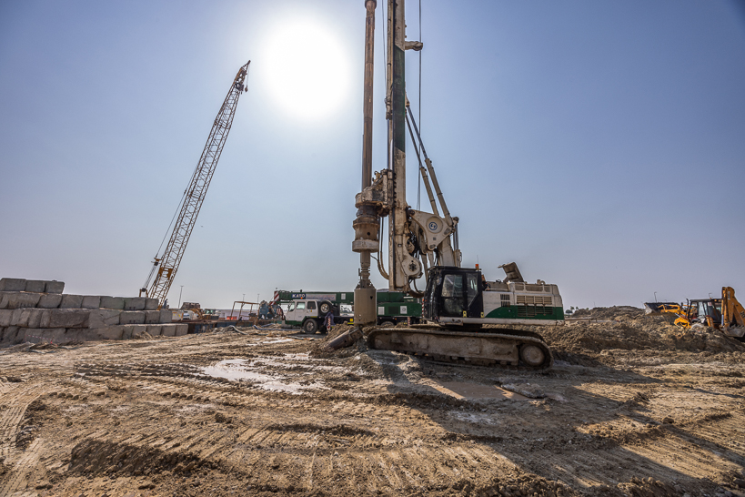 Beach Walk Residence A construction site featuring a large drilling machine, cranes, and heavy machinery under a bright sun.