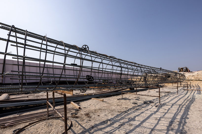 Beach Walk Residence A construction site featuring a large, coiled rebar frame, surrounded by loose steel and sand under a clear sky.