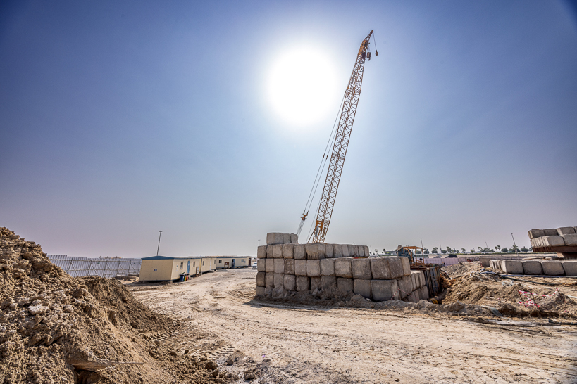 Beach Walk Residence Construction site with a crane, piles of building materials, and clear blue sky under bright sunlight.