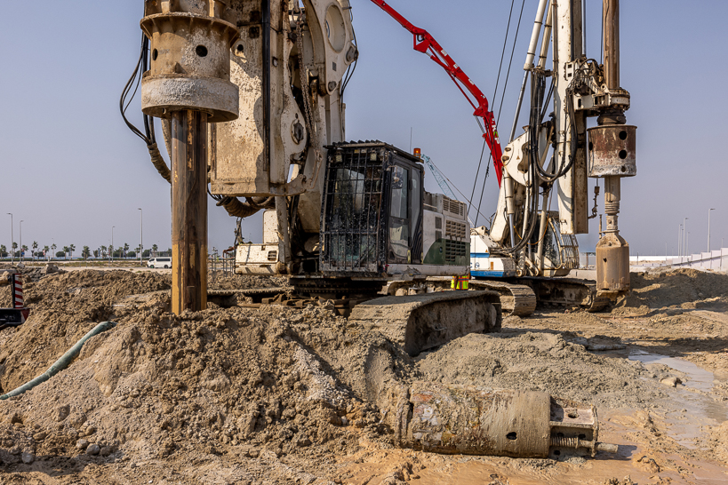 Beach Walk Residence A large drilling rig on a construction site, surrounded by earth and machinery, under a clear blue sky.