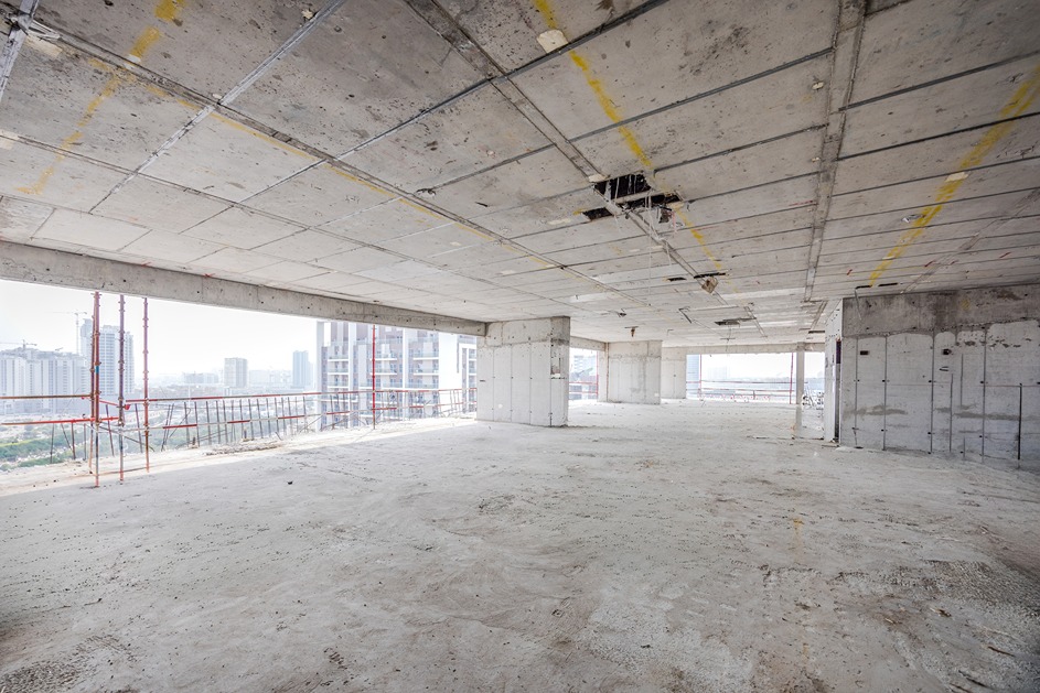 Pearl House By Imtiaz Empty interior of a newly constructed building with concrete floors and walls, large windows revealing a city view.