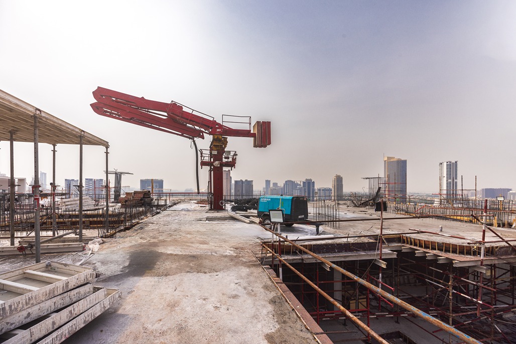 Pearl House By Imtiaz A construction site with a large red crane, scaffolding, and materials, overlooking a city skyline.