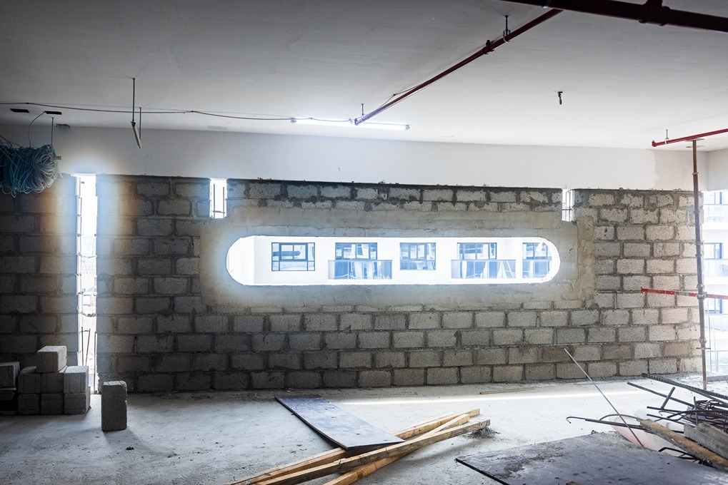 Pearl House By Imtiaz An unfinished wall in a construction site features a rectangular window revealing an exterior view.