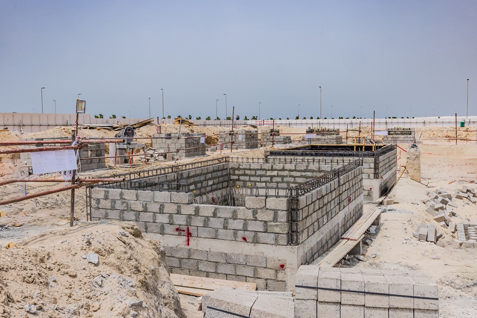 Beach Walk Residence Construction site with partially built concrete structures and materials scattered on sandy ground under a clear sky.