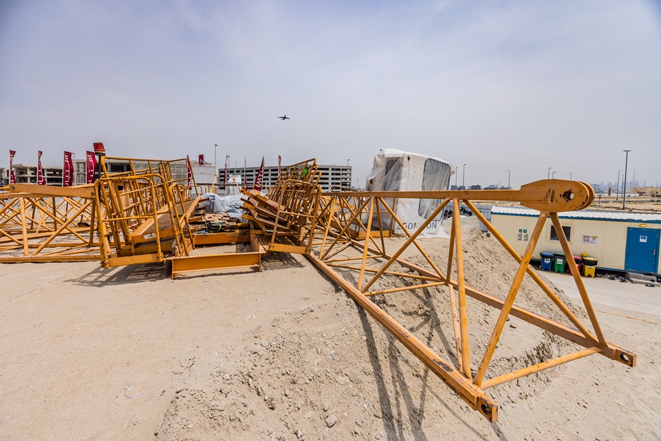 Beach Walk Residence A construction site featuring yellow crane parts scattered on sandy ground with an airplane flying overhead.