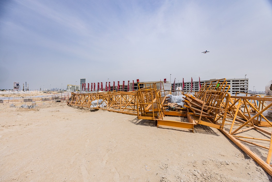 Beach Walk Residence Construction site with yellow cranes, scattered materials, and an airplane flying overhead against a clear sky.