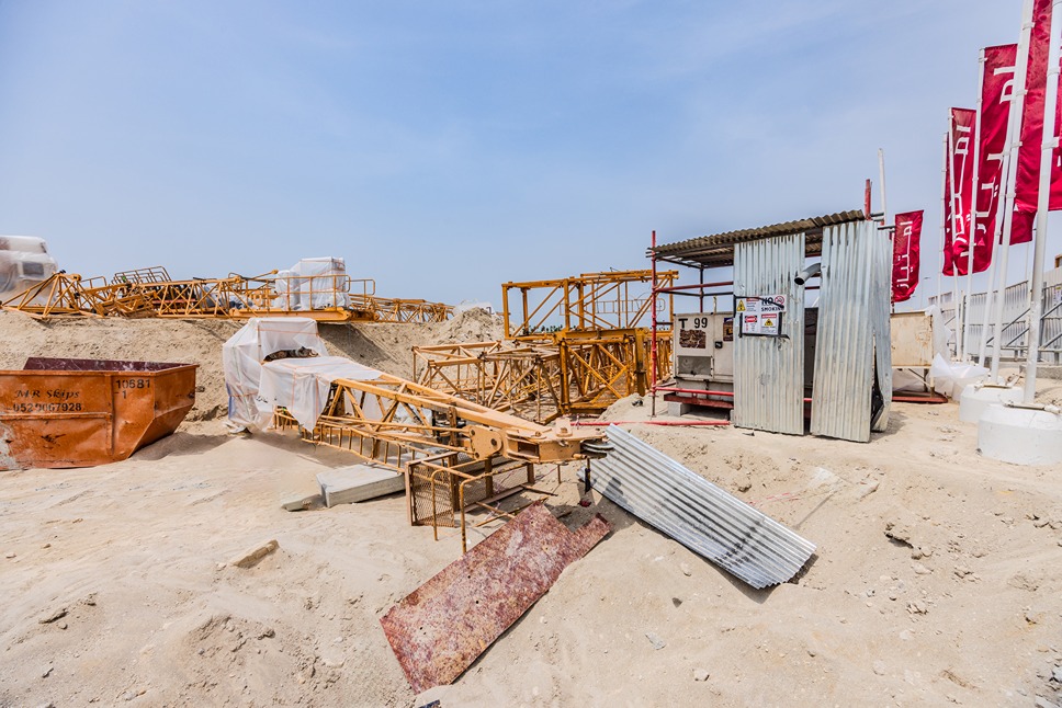 Beach Walk Residence Construction site featuring orange cranes, equipment, and sand, under a clear blue sky with some red flags.