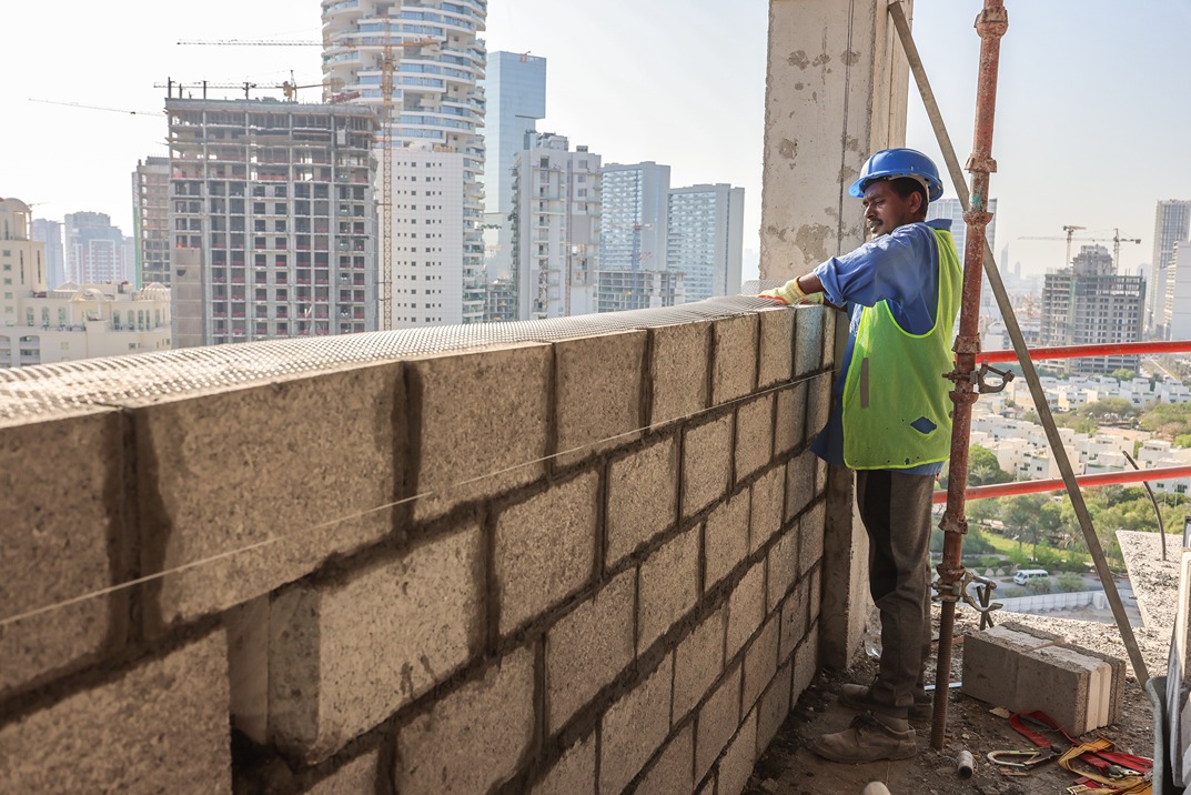 Pearl House By Imtiaz A construction worker in a blue helmet builds a wall of concrete blocks on a high-rise building site.