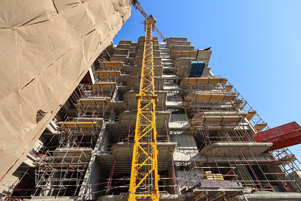Pearl House By Imtiaz A tall construction site with scaffolding and a crane against a clear blue sky.