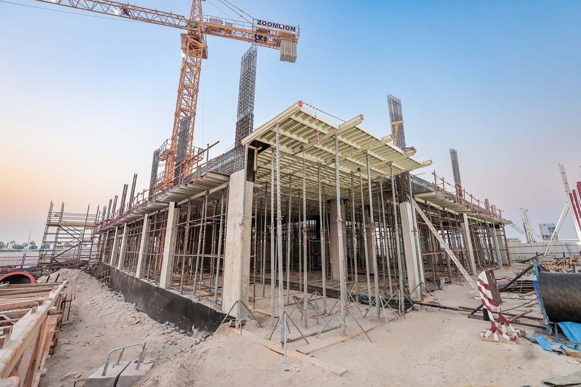Beach Walk Residence Construction site featuring a partially built structure with scaffolding, concrete pillars, and a crane in the background.