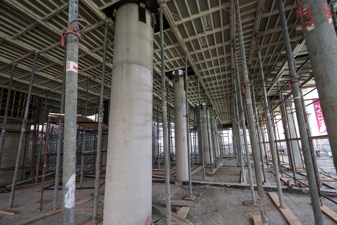 Beach Walk Residence Construction site interior featuring concrete columns, scaffolding, and a ceiling framework. Dusty ground visible.