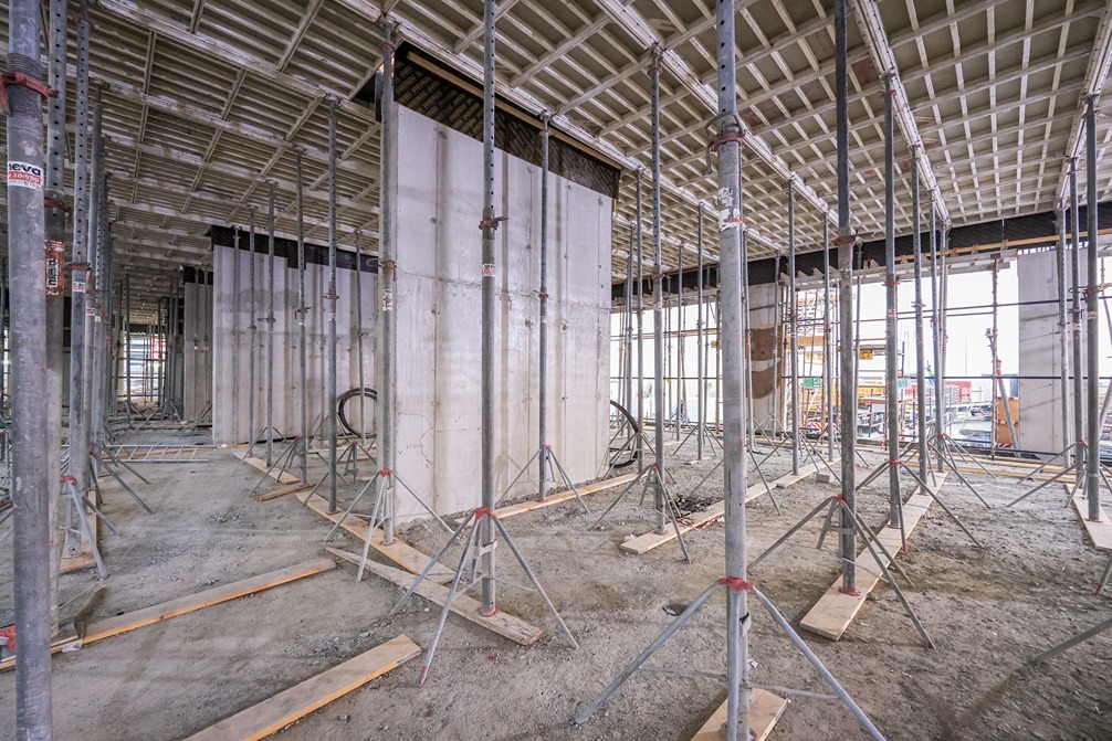 Beach Walk Residence A construction site interior showing exposed concrete walls, scaffolding, and a gravel floor under natural light.