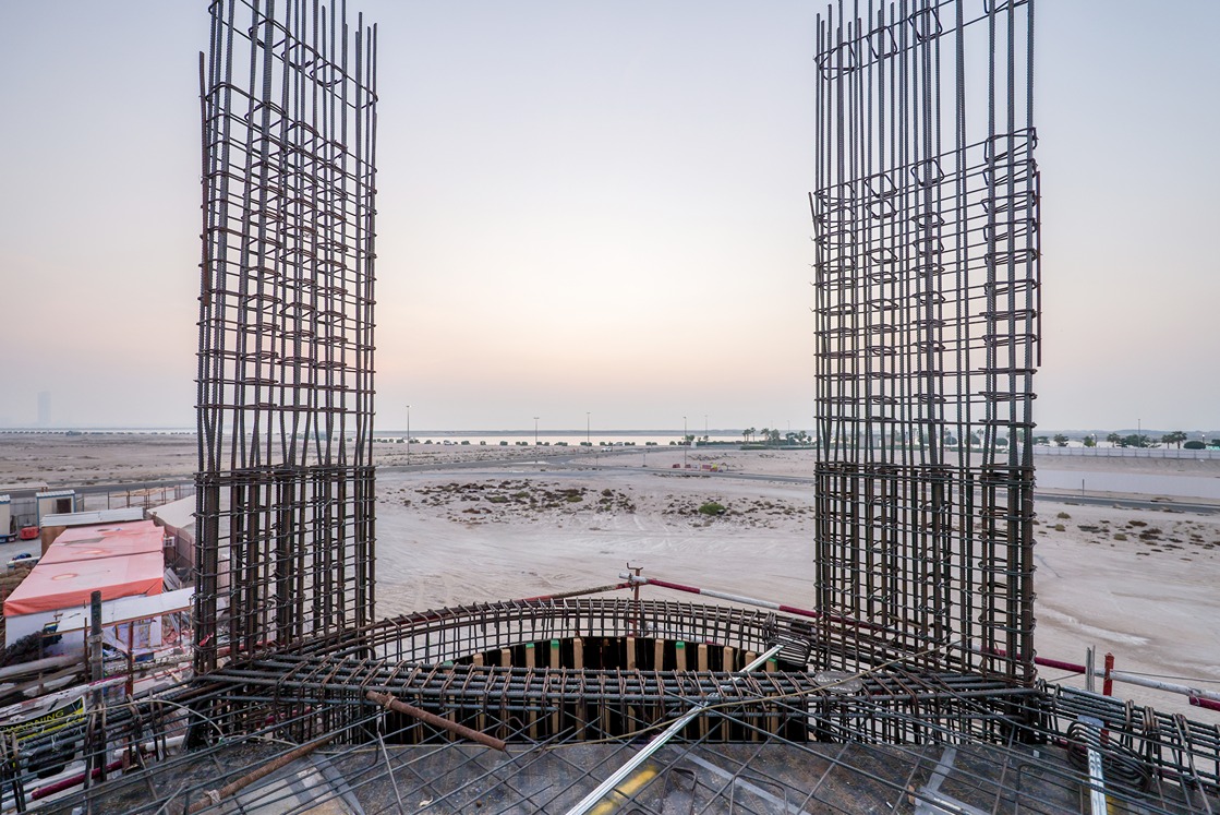 Beach Walk Residence Construction site view featuring rebar framework and scaffolding overlooking a sandy landscape at dusk.