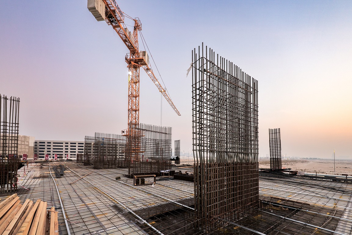 Beach Walk Residence A construction site featuring a large crane, metal frameworks, and concrete foundations under a pastel sky.