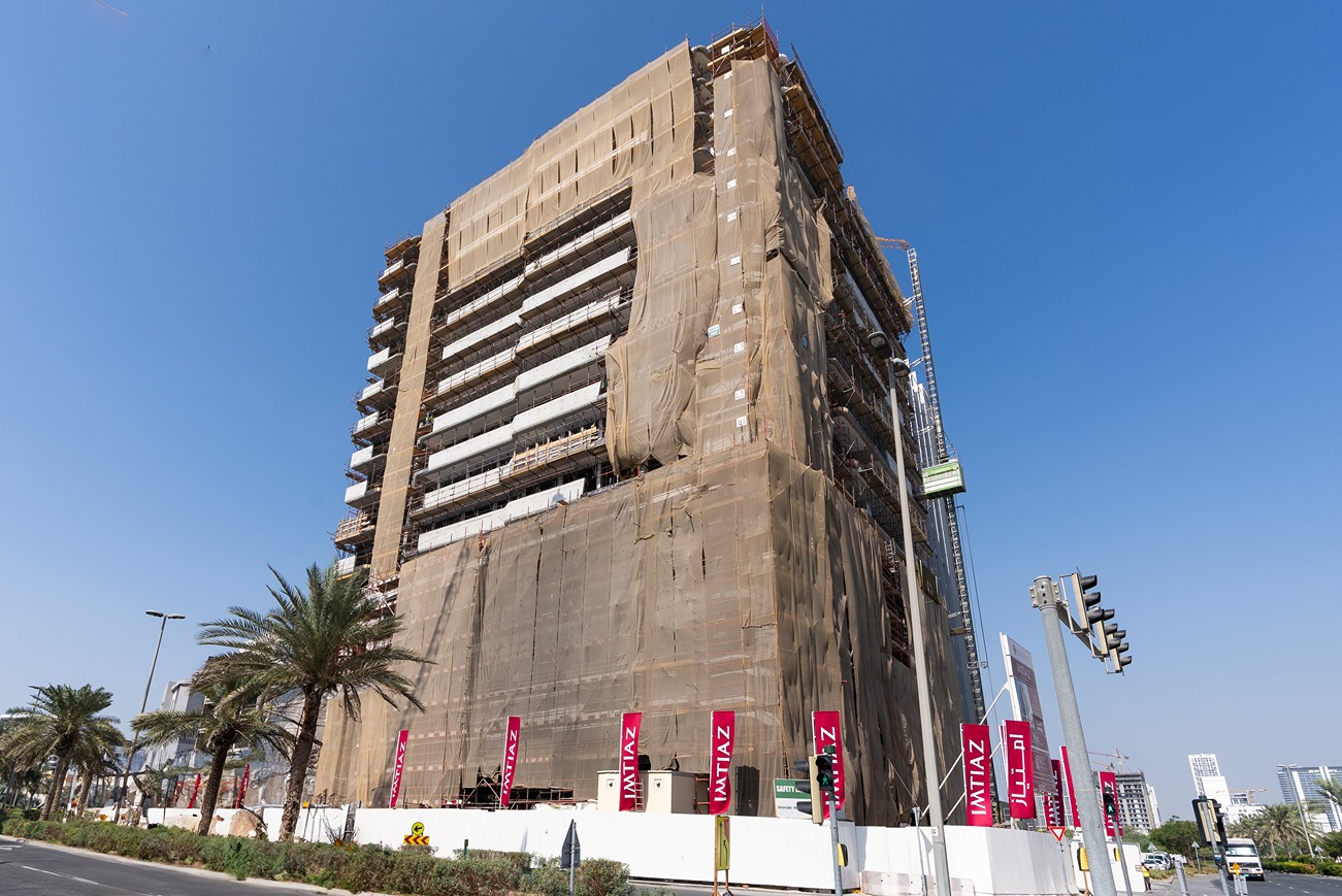 Pearl House By Imtiaz A tall building under construction, wrapped in protective fabric, with palm trees and signage nearby.
