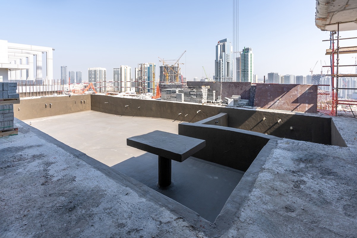 Pearl House By Imtiaz A construction site featuring a large, empty pool area with a surrounding city skyline in the background.