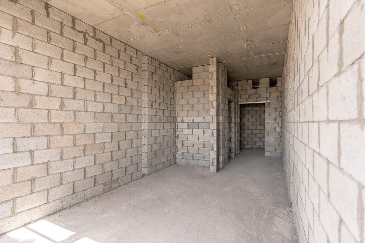 Pearl House By Imtiaz An unfinished room with gray block walls and a concrete floor, featuring multiple doorways and a ceiling.