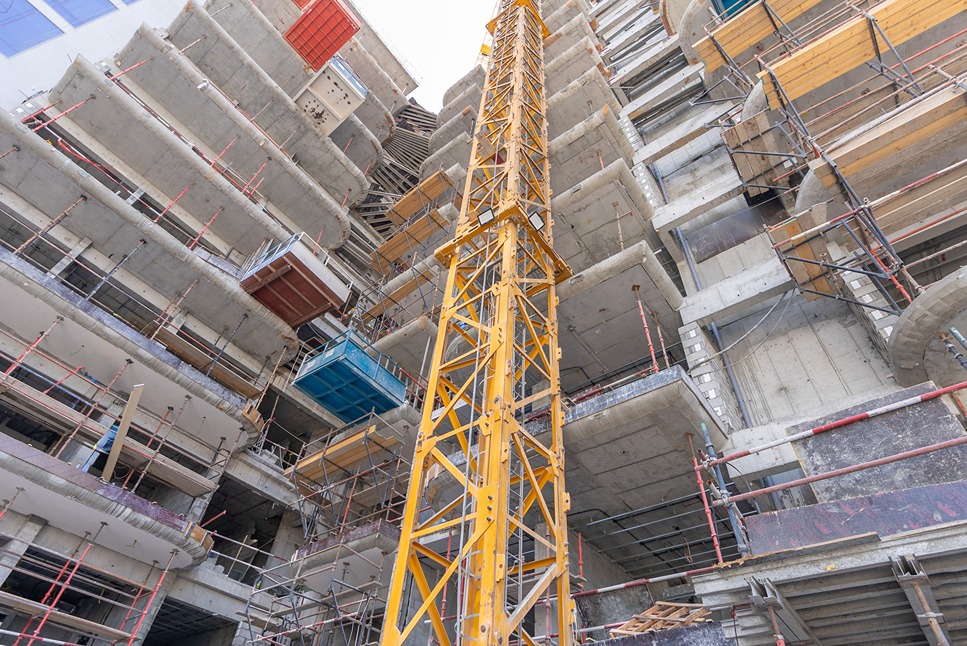Pearl House By Imtiaz A tall yellow construction crane next to a concrete building under construction with scaffolding and platforms.