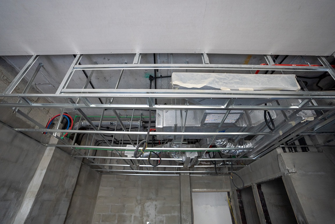Pearl House By Imtiaz A ceiling framework with exposed ducts, pipes, and wires in an unfinished construction area.