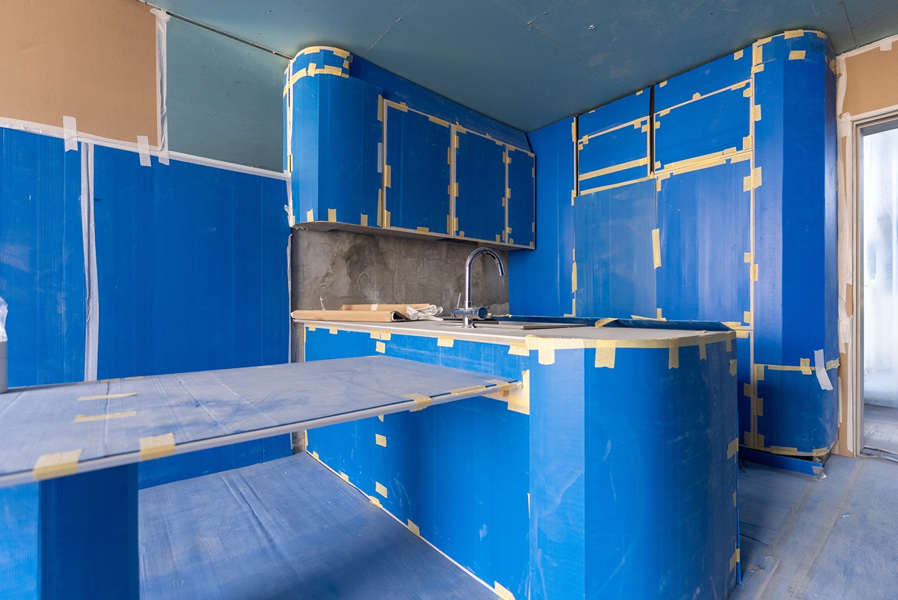 Pearl House By Imtiaz A partially renovated kitchen featuring blue protective coverings on cabinets and surfaces, with visible concrete walls.