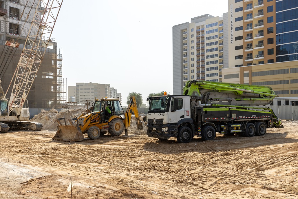 Cove Edition I By Imtiaz 1 Construction site with heavy machinery including a yellow backhoe, a concrete pump truck, and a crane.