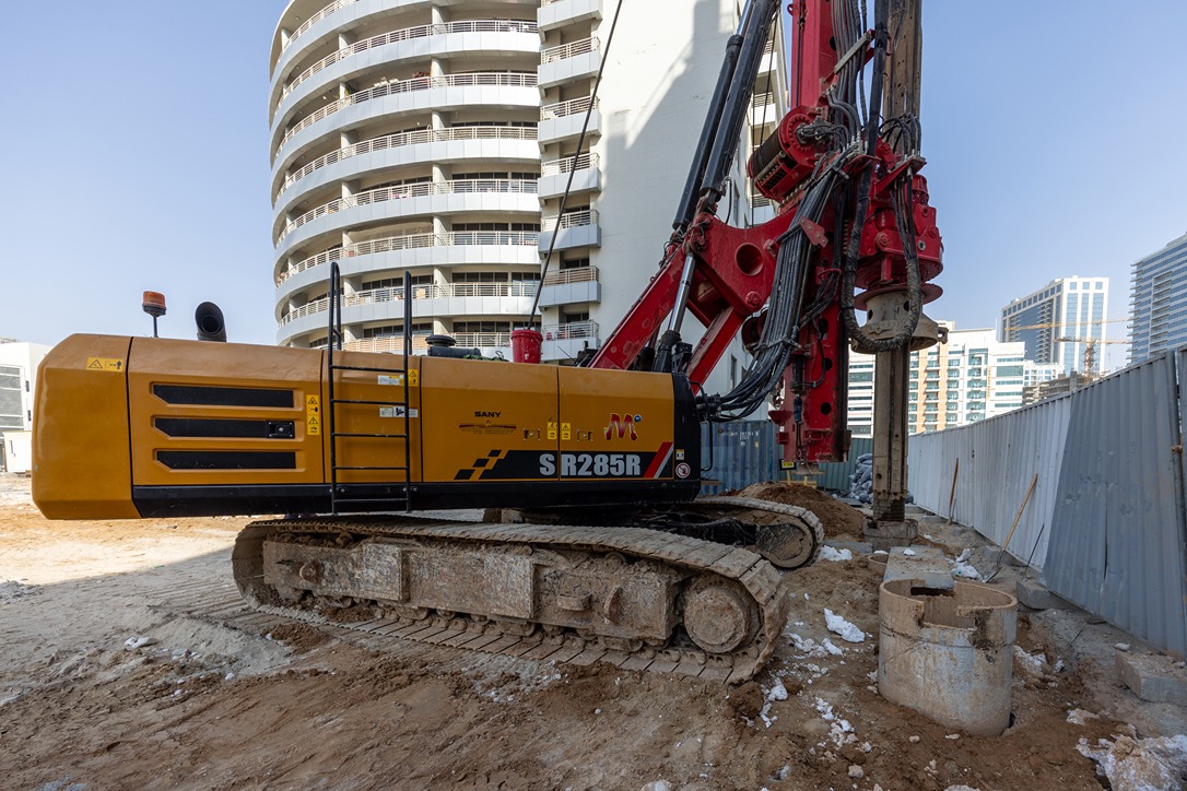 Cove Edition I By Imtiaz 1 A large yellow and red construction drill on a building site, with modern apartments in the background.