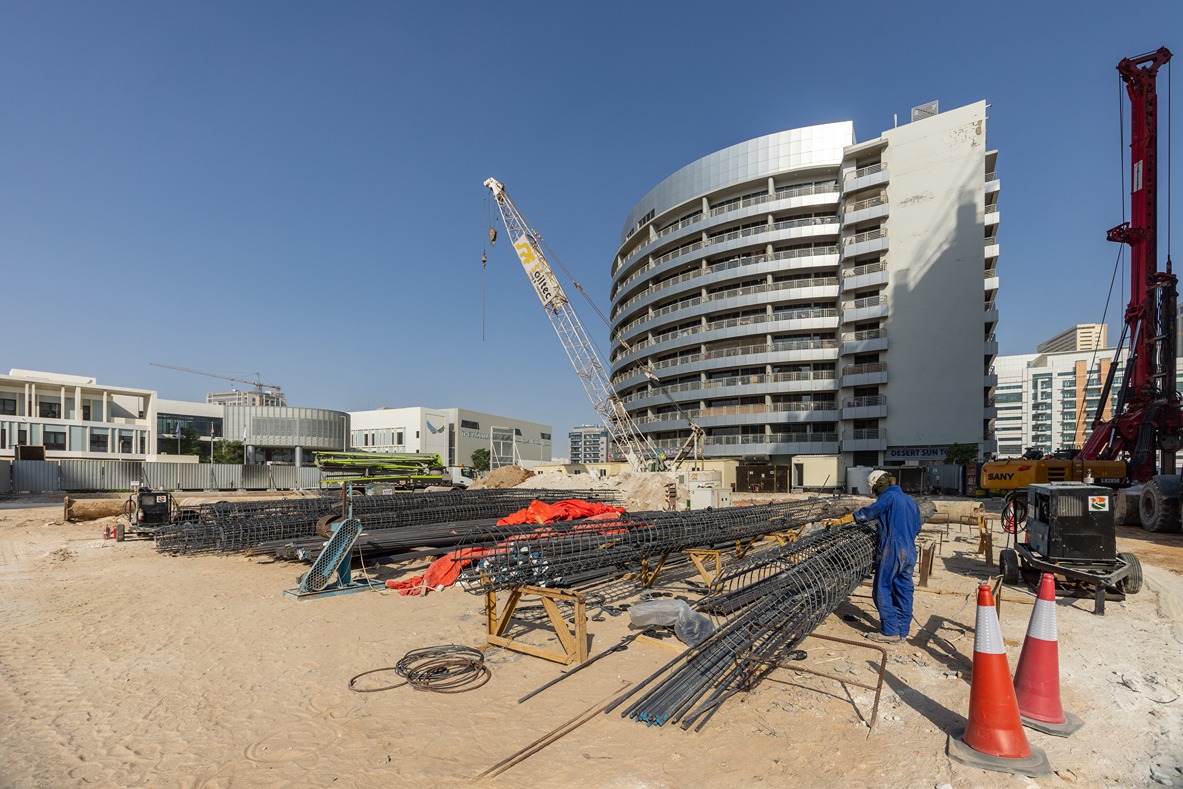 Cove Edition I By Imtiaz 1 Construction site featuring steel rebar, cranes, and a building in progress under a clear blue sky.