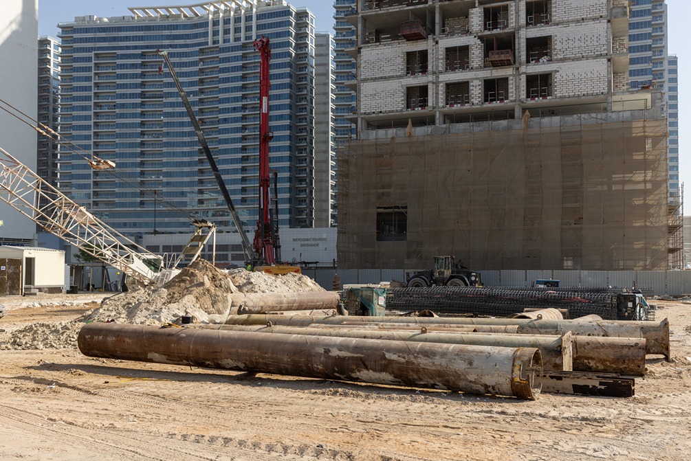 Cove Edition I By Imtiaz 1 Construction site with heavy machinery, pipes, and partially built buildings in an urban setting.