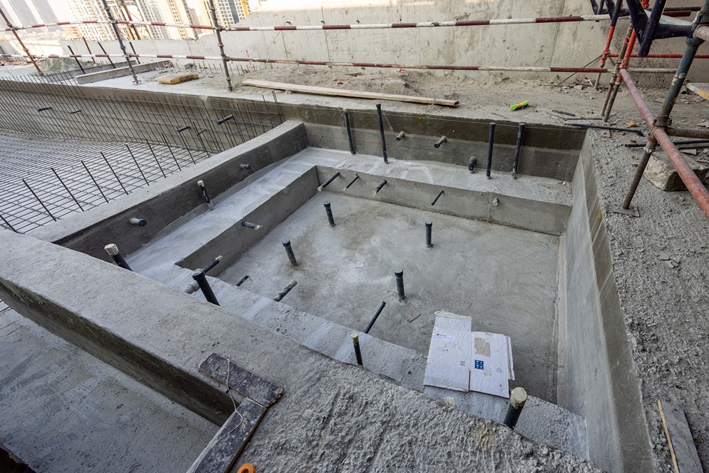 Pearl House By Imtiaz View of a concrete construction site with a foundation pit and protruding pipes for future installations.