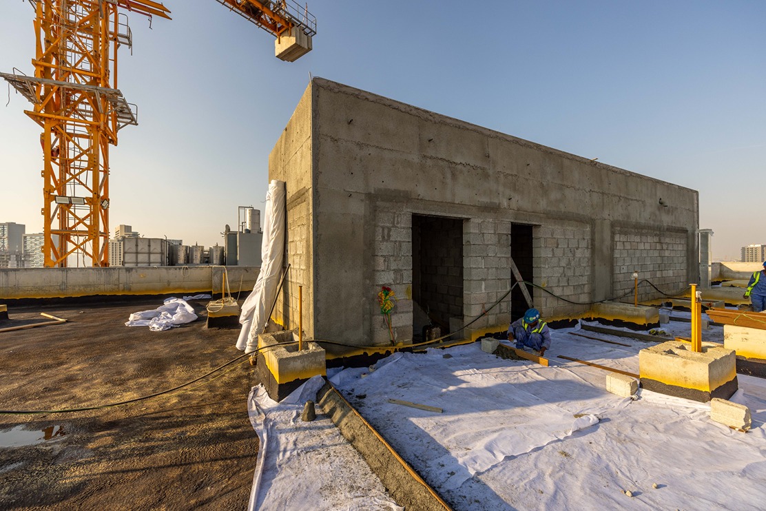 Pearl House By Imtiaz Construction workers are on a rooftop with a crane nearby, working on building foundations and walls.