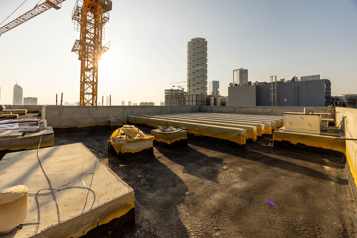 Pearl House By Imtiaz Construction site rooftop with yellow and black surfaces, crane, and city buildings under a clear sky.