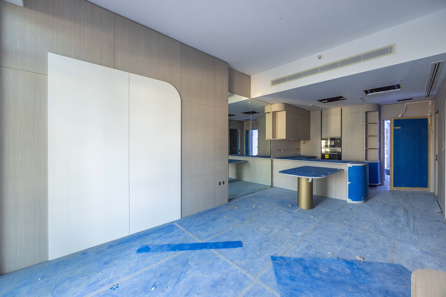 Pearl House By Imtiaz A modern, unfinished kitchen with light wood cabinetry, blue flooring, and a central blue table with a gold base.