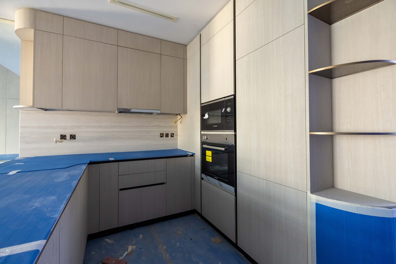 Pearl House By Imtiaz Modern kitchen with light wood cabinets, blue countertops, and built-in appliances, including an oven and microwave.