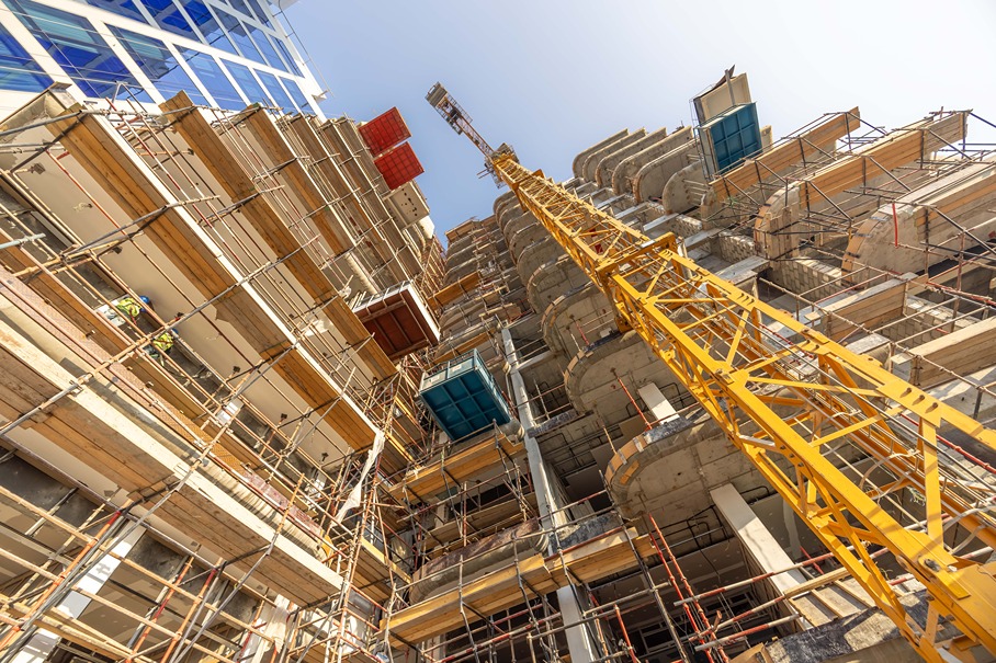 Pearl House By Imtiaz Construction site with a skyscraper under development, featuring scaffolding and a yellow crane against a clear sky.