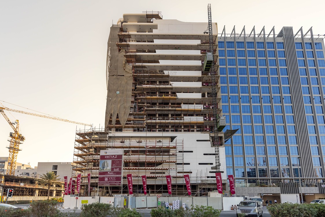 Pearl House By Imtiaz A partially constructed building with scaffolding, nearby a modern glass structure, and construction signage visible.