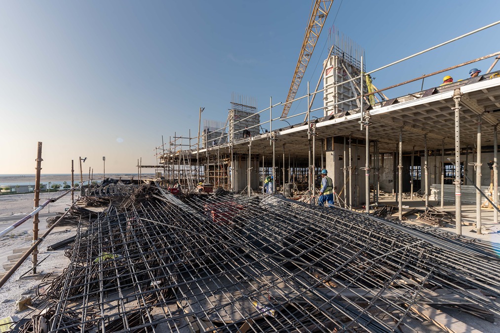 Beach Walk Residence Construction site featuring scaffolding, steel rebar, workers, and a clear sky in the background.