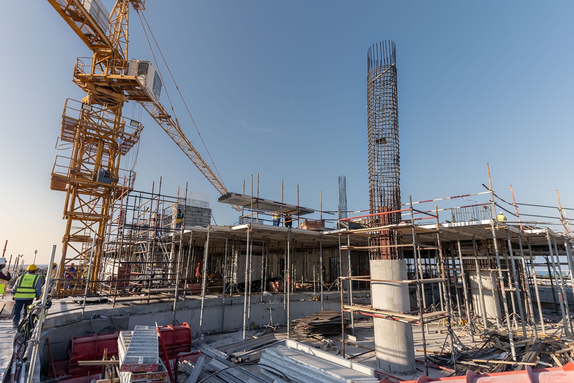 Beach Walk Residence Construction site with cranes, scaffolding, workers, and rebar structures under a clear blue sky.