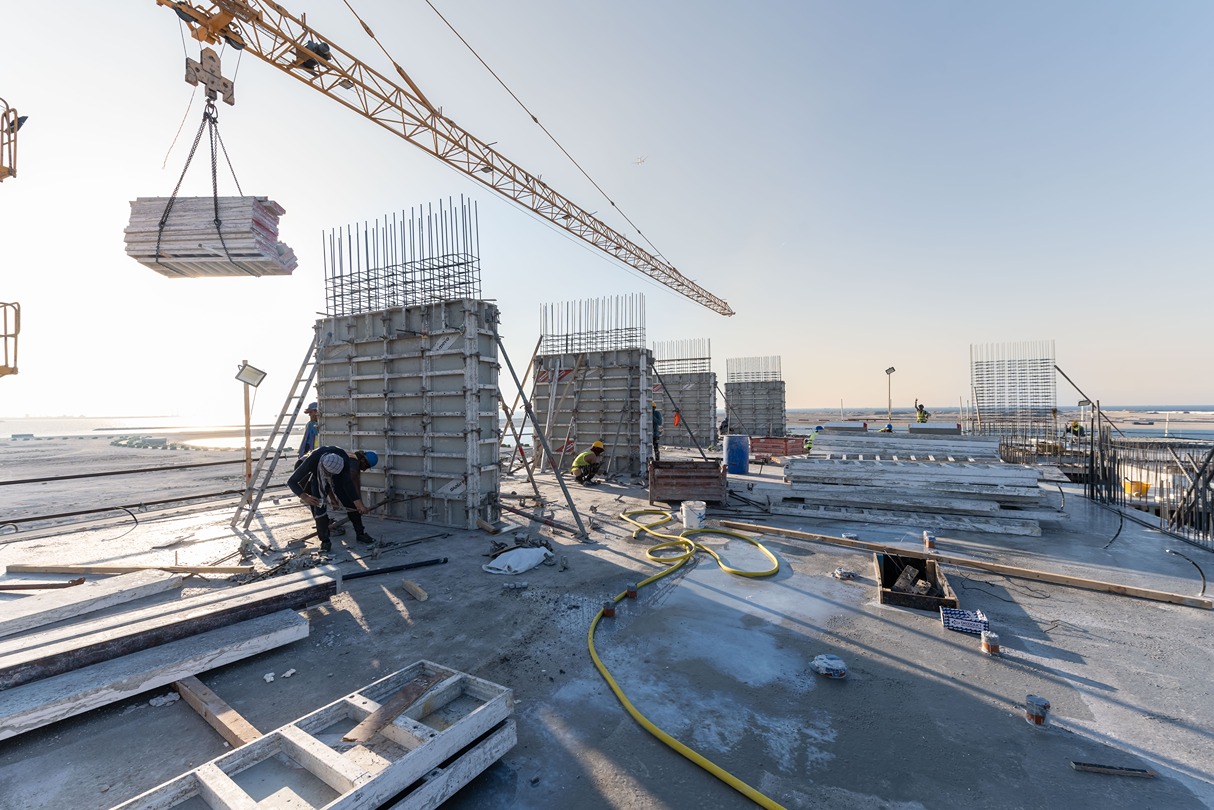 Beach Walk Residence Construction workers on a rooftop site, with cranes, concrete forms, and reinforcing bars under a clear sky.