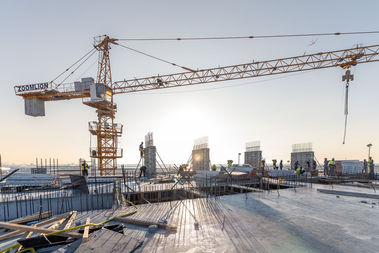 Beach Walk Residence Construction site at sunset with a crane, workers in safety gear, and rebar structures being erected.