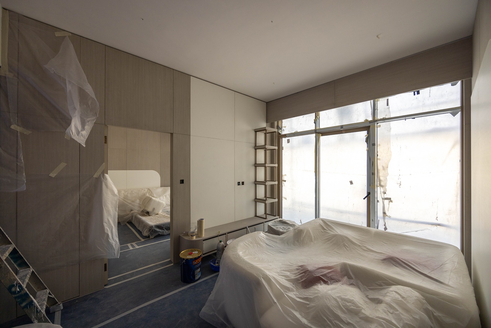 Pearl House By Imtiaz A partially renovated room with minimalist design, covered furniture, and a large window covered with plastic.