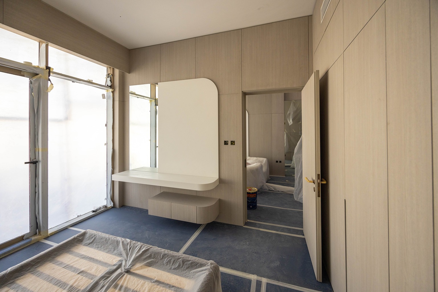 Pearl House By Imtiaz A modern, minimalist room with large windows, light wooden walls, and a vanity table in soft tones.