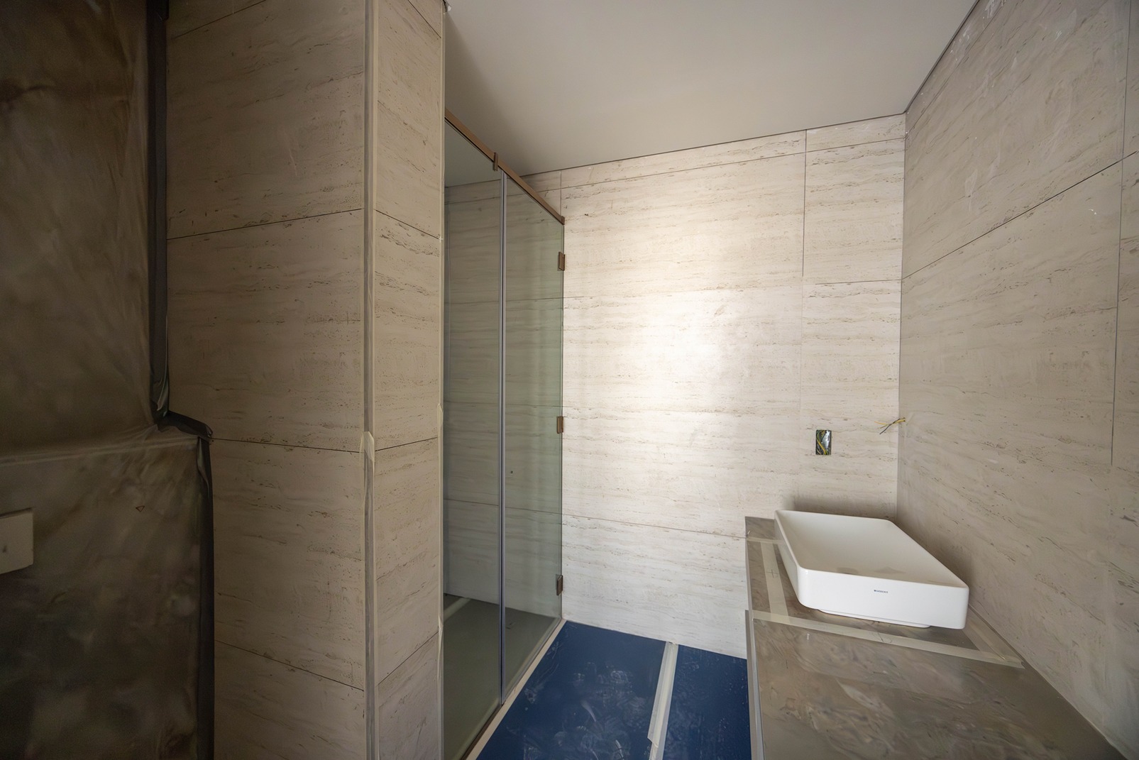 Pearl House By Imtiaz A modern bathroom featuring a glass shower enclosure, white sink, and light stone walls.