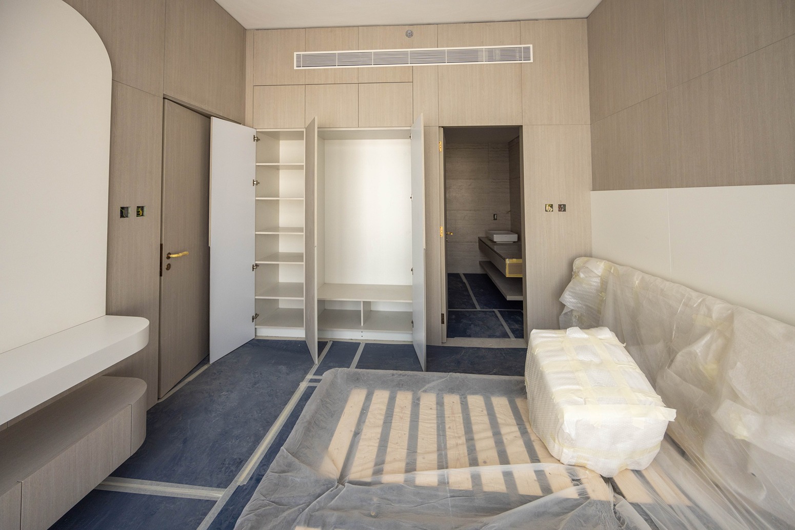 Pearl House By Imtiaz A modern, minimalist room featuring a couch with protective covering, open closet, and a bathroom door visible.