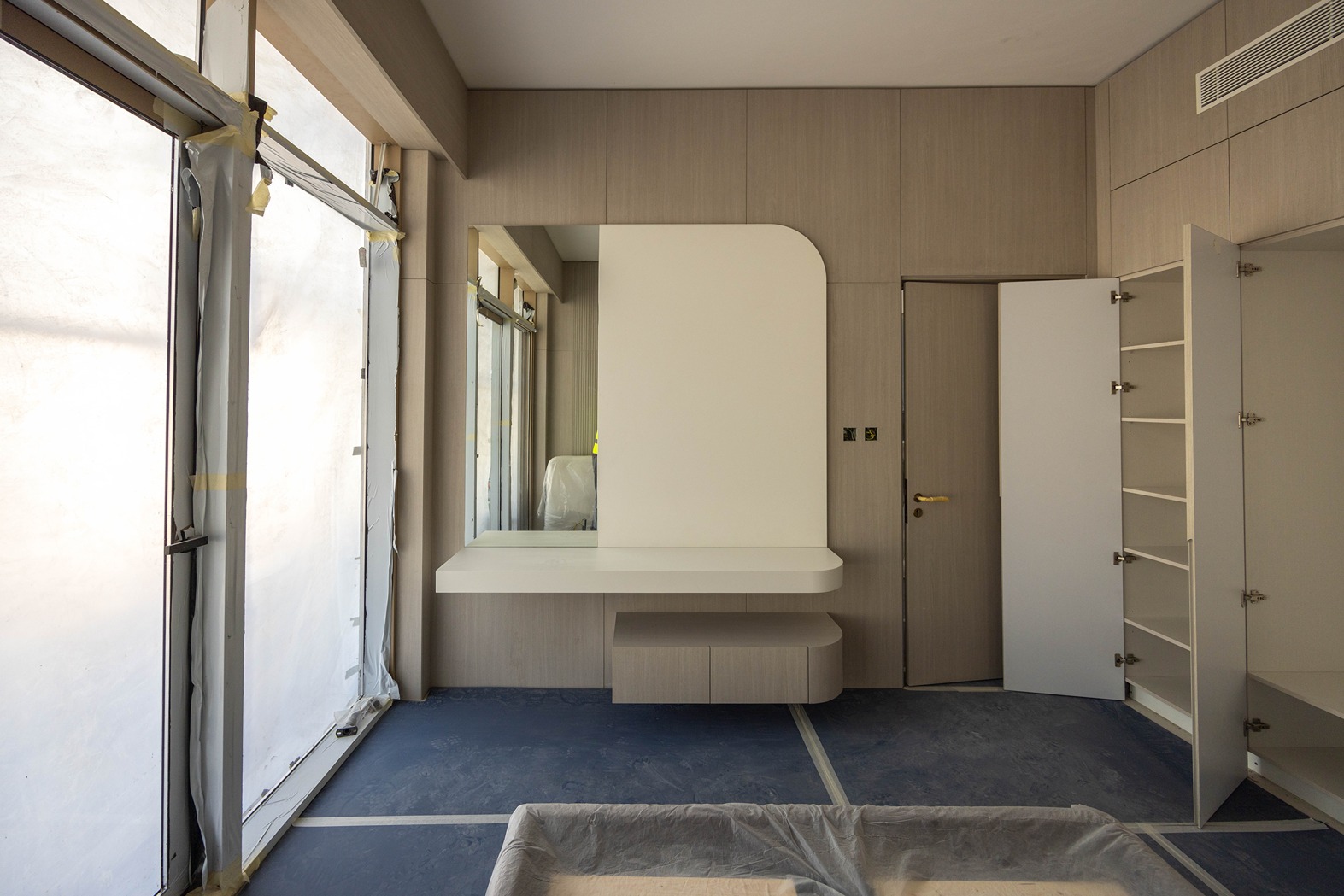 Pearl House By Imtiaz A modern, unfinished room featuring a large mirror, storage shelves, and plastic-covered windows.