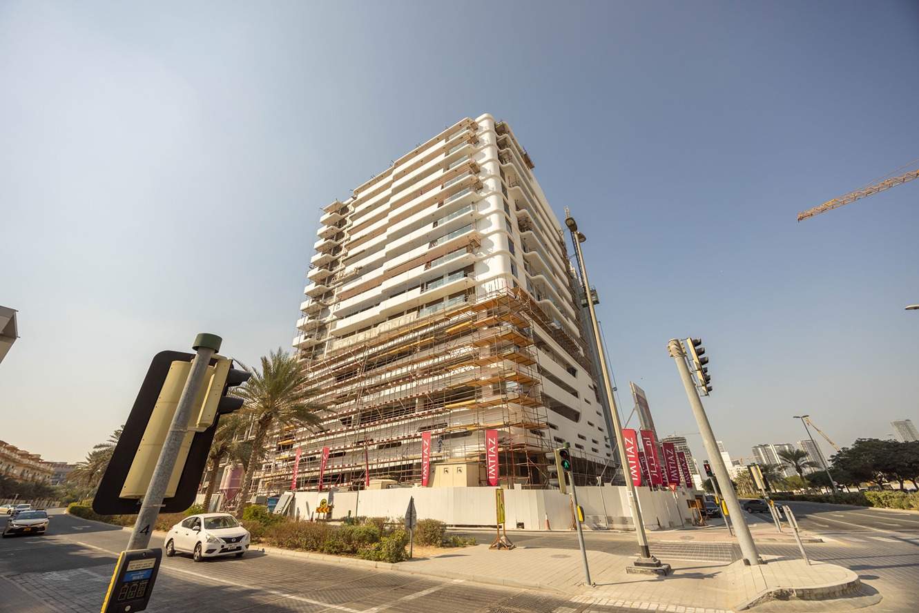 Pearl House By Imtiaz A construction site with a partially finished modern building, traffic lights, and palm trees, in a clear sky.
