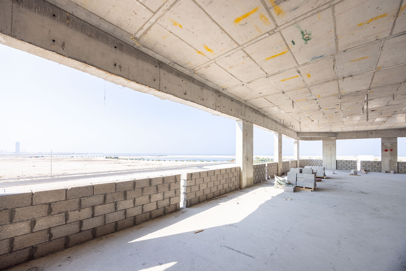 Beach Walk Residence Interior of an unfinished building with concrete walls and large windows offering a view of the landscape outside.